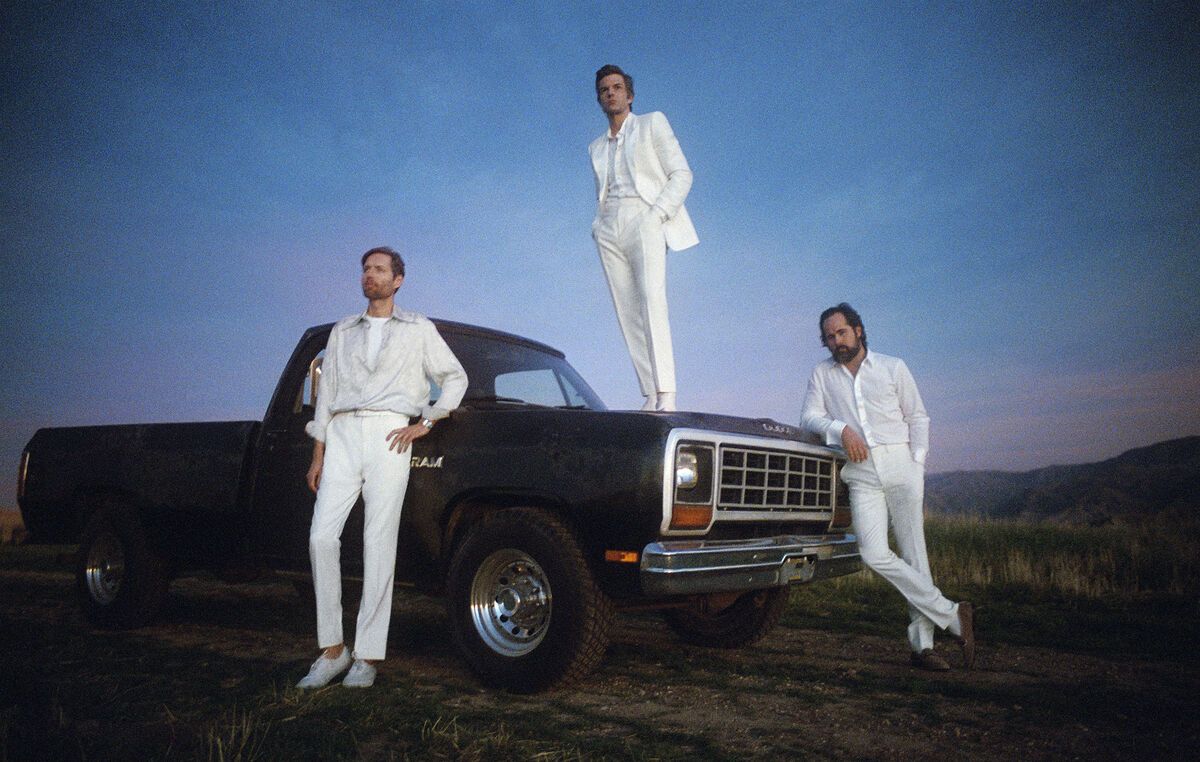 Ketiga personel The Killers berpose dengan sebuah mobil dengan memakai pakaian serba putih